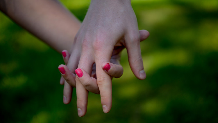 Kaksi kättä sormet limittäytyneenä yhteen, toisen käden kynsissä pinkki kynsilakka