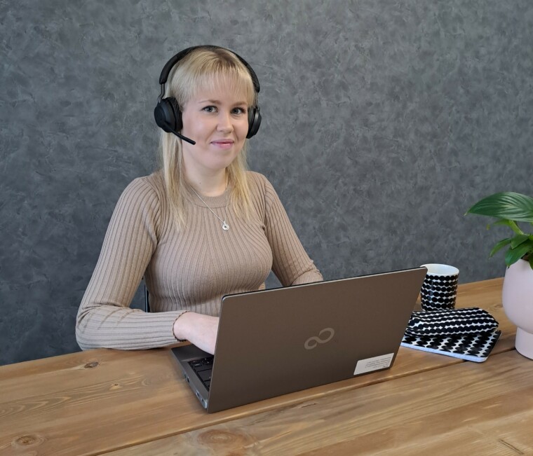 Eloisan sairaanhoitaja Salla-Mari Kilpeläinen istuu tietokoneen ääressä kuulokkeet korvissa ja katsoo kameraan päin