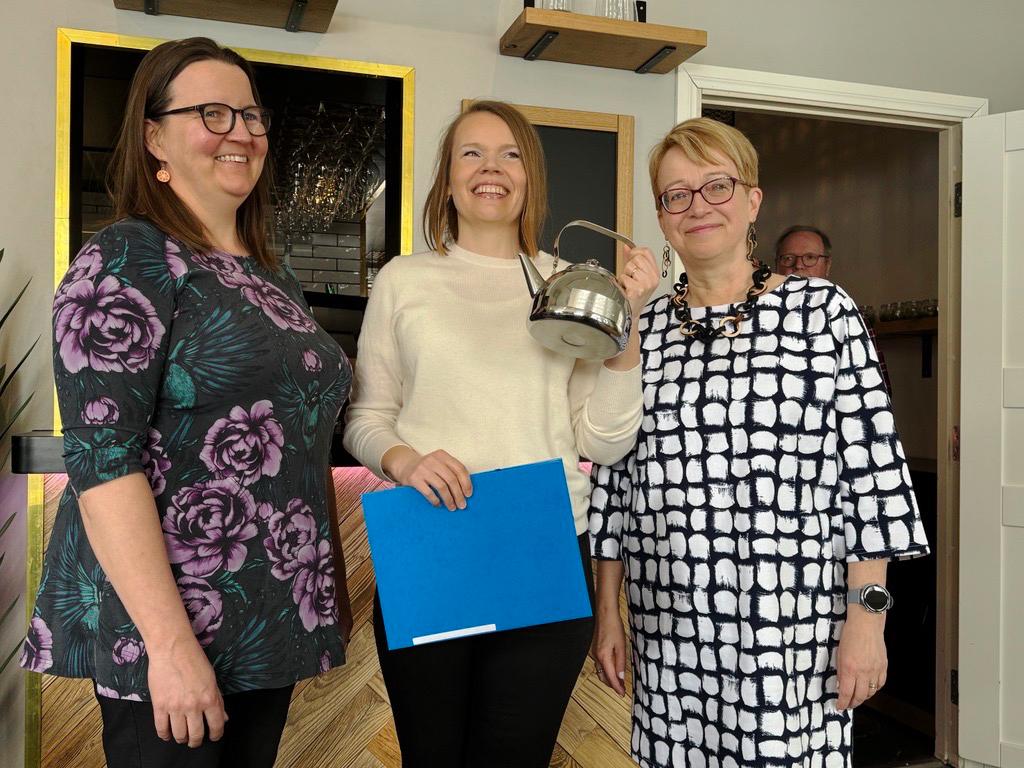 kuvassa kolme naista palkitsemistilaisuudessa. Keskiimmäinen pitää käsissään metallista kahvipannua.