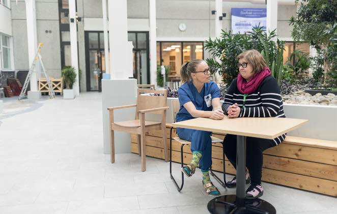 Kuvassa Tiia Kokkonen ja Tiina Aalto istuvat pöydän ääressä Savonlinnan keskussairaalan kansalaistorilla ja keskustelevat.