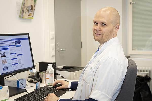 Eloisassa lääkärinä työskentelevä Jukka Siimes lääkärintakissaan työkoneen äärellä. Hän on yksi SYTY-koulutuksessa osallistuvista yleislääketieteeseen erikoistuvista lääkäreistä.