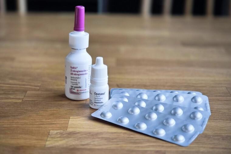allergialääkkeitä puisella pöydällä, nenäsuihkepullo, silmätippapullo ja tablettiliuskoja