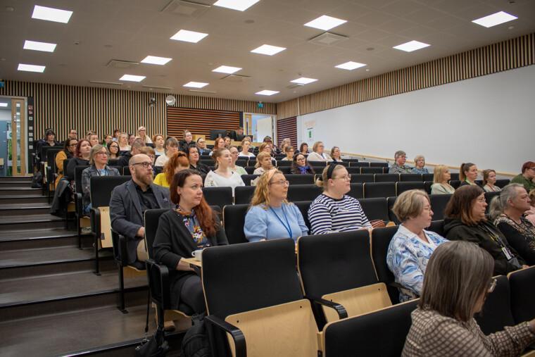 Auditoriossa ihmisiä istumassa ja odottamassa ohjelman alkua.