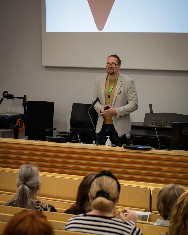 Santeri Seppälä seisoo auditorion näyttämöllä ja puhuu. Edessä ihmiset kuuntelevat.