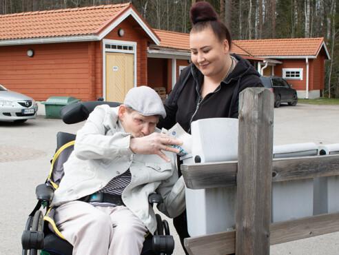 Mies istuu pyörätuolissa ja ottaa sanomalehteä avoinna olevasta postilaatikosta. Hänen takanaan seisoo nainen, joka pitää postilaatikon kantta auki ja katsoo miestä hymyillen.