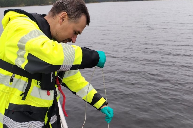 LVV:n edustaja keltaisessa huomiotakissa ottamassa vesinäytettä suojahanskat kädessä.