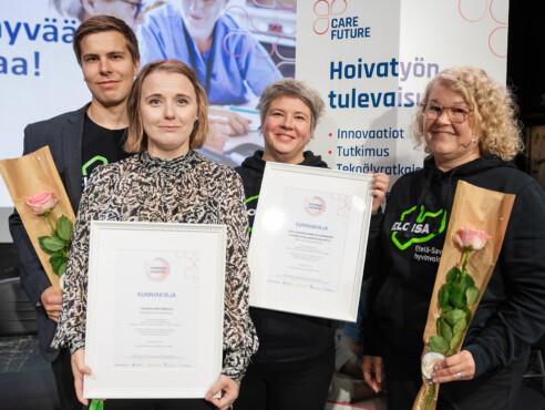 neljä henkilöä käsissään kaksi kunniakirjaa ja ruusut