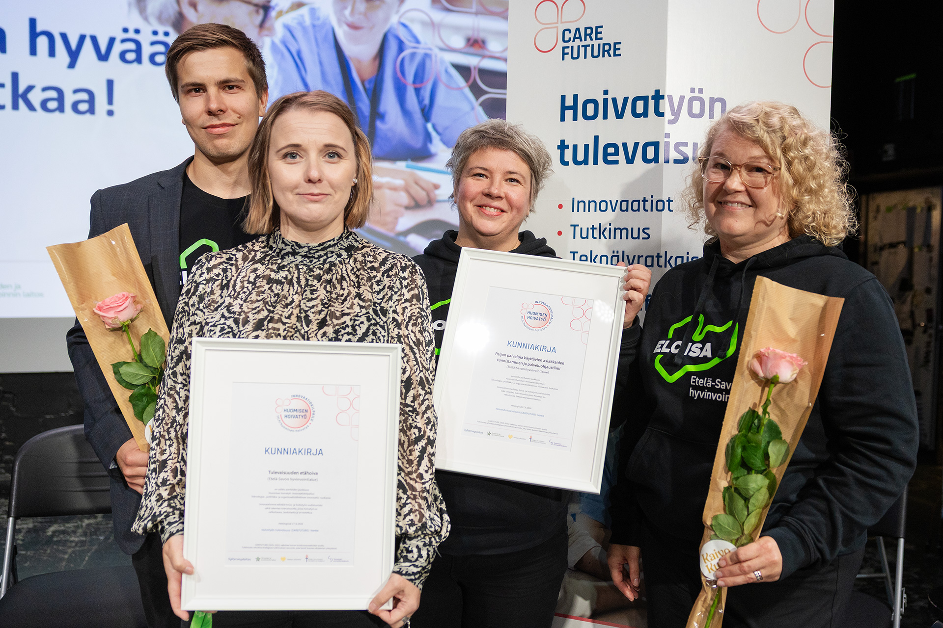 neljä henkilöä käsissään kaksi kunniakirjaa ja ruusut