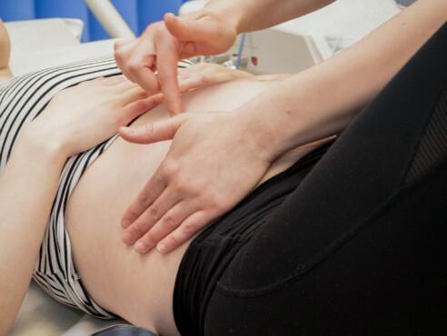lähikuva raskaana olevan vatsasta jonka päällä kätilön kädet