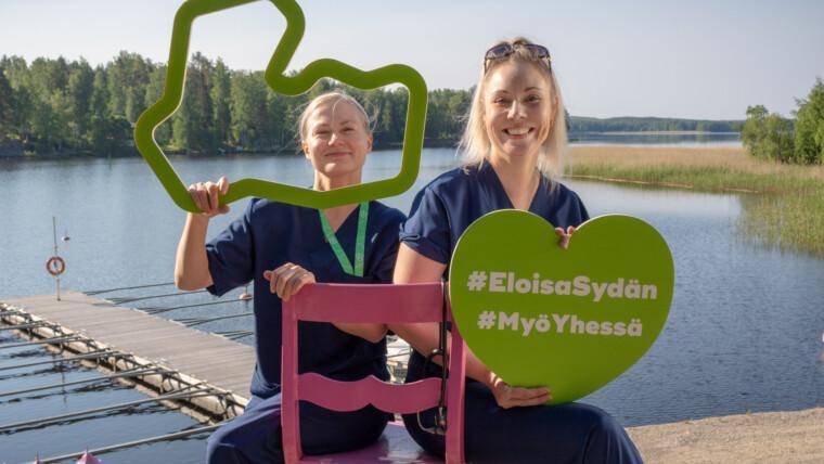 Kaksi siniasuista sairaanhoitajanaista istuvat tuolilla kallioisella rannalla